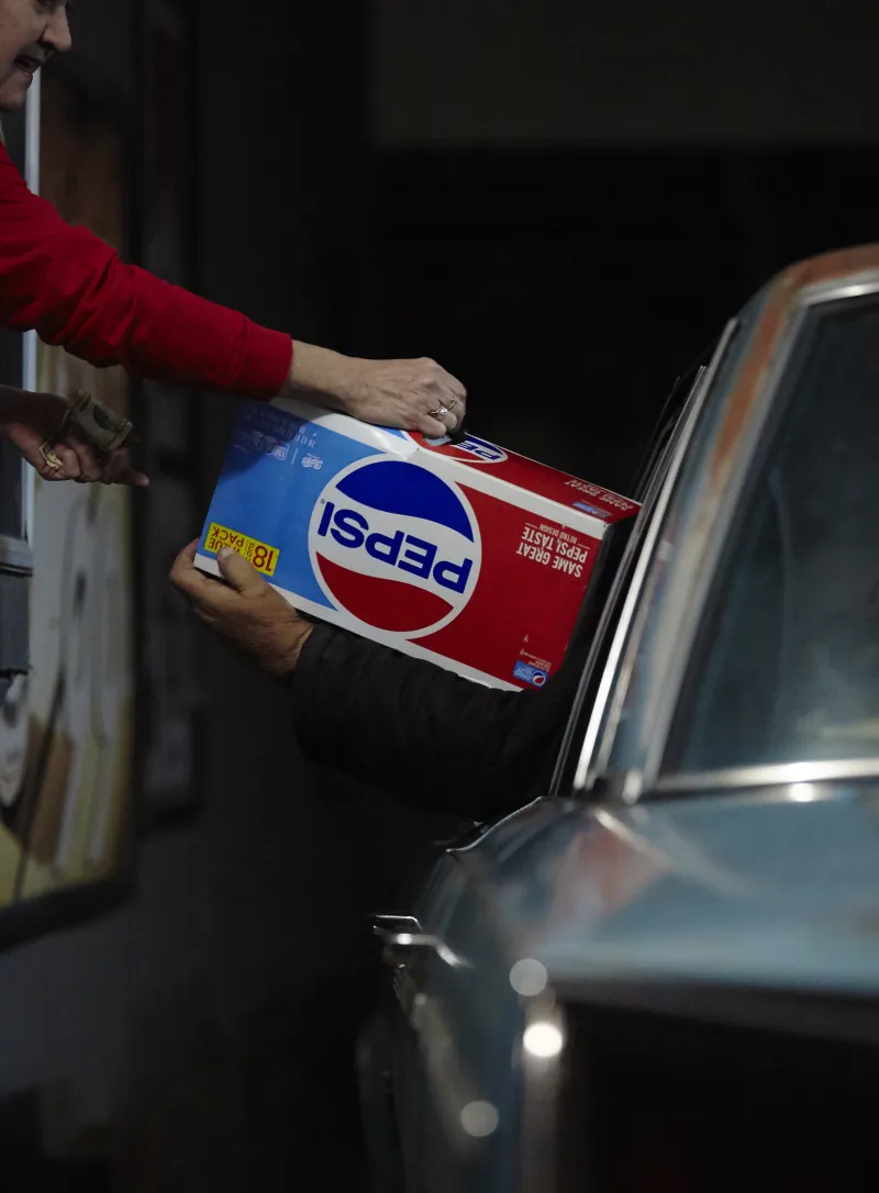 Patty Frazee, a long-time employee of Cee Dee, a drive-thru liquor and grocery in Chauncey, Ohio, hands a 18-pack of Pepsi to Frank Kelsey, a life-long resident of Chauncey in exchange for a ten-dollar-bill. “I like to drink them every day, I also like to give them away!” Frank says as he sits in the drivers seat of his light blue 1966 Dodge Polaris.