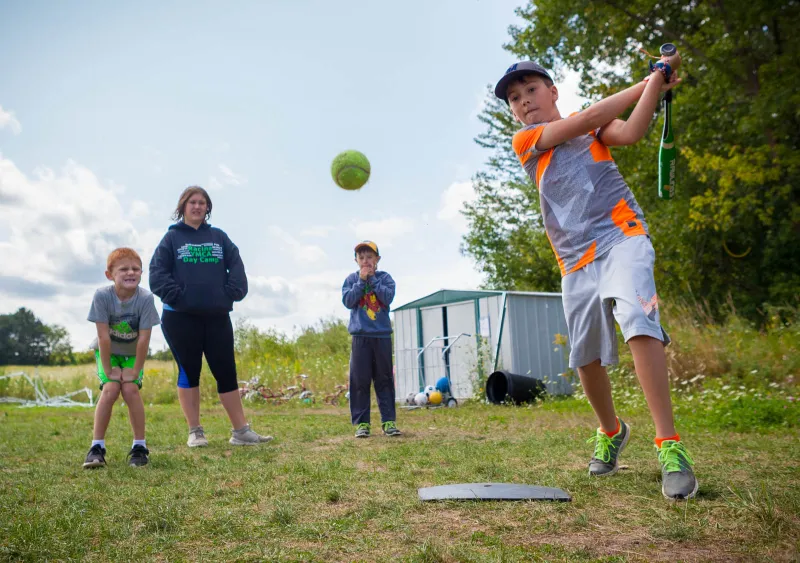 Gus Etes swings to hit an incoming tennis ball during a game of baseball at a Sealed Air Branch YMCA summer camp in Mount Pleasant.