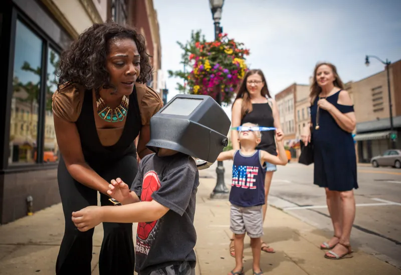 Dwana Carson helps passerby Tommy Takerian view the solar eclipse through a welding mask on Aug. 21. Carson invited any Main Street passerby to look through the mask as she stood outside her clothing shop, R&D Executive.